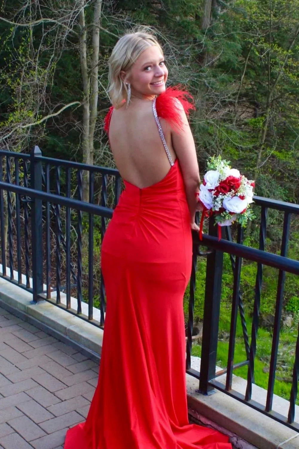 Red V-neck mermaid prom dress featuring luxury diamond straps, feather accents, and an open back.