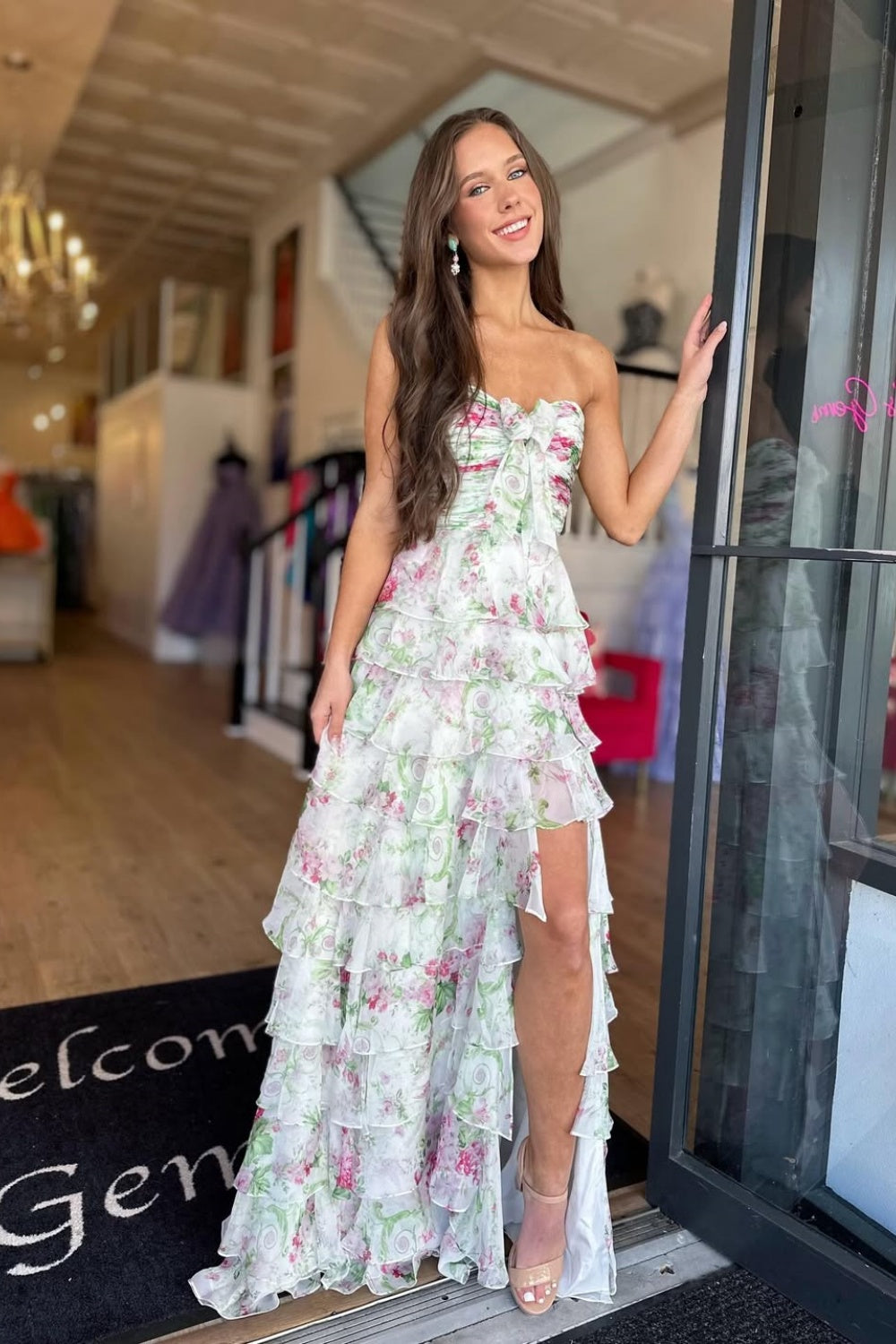 Floral print chiffon A-line prom dress featuring ruffles, a side slit, and a bow front detail.