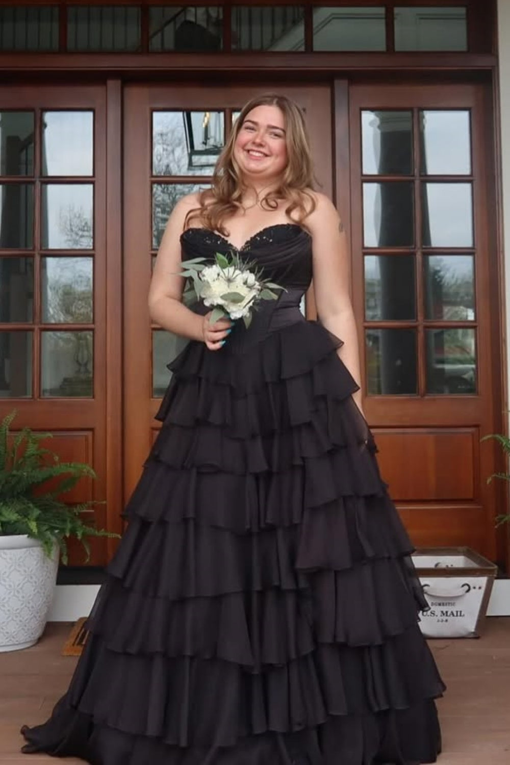Black sweetheart A-line tiered prom gown featuring intricate lace appliques and a voluminous layered skirt.