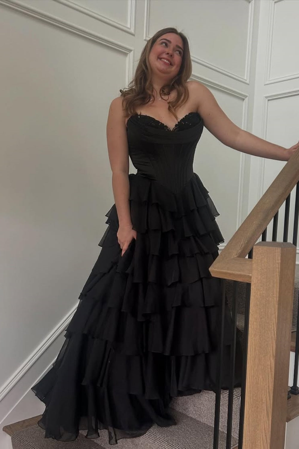 Black sweetheart A-line tiered prom gown featuring intricate lace appliques and a voluminous layered skirt.