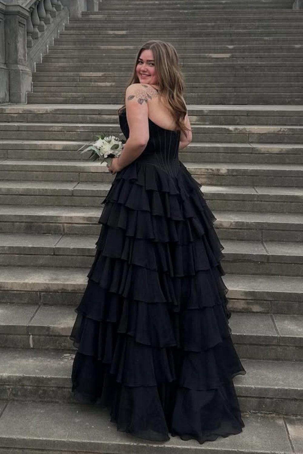 Black sweetheart A-line tiered prom gown featuring intricate lace appliques and a voluminous layered skirt.