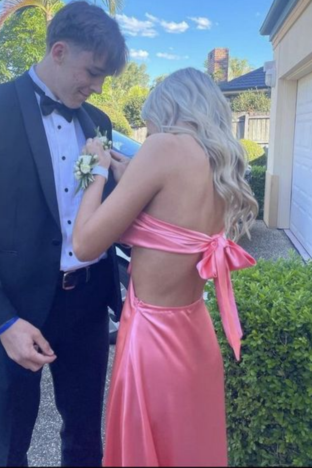 Blush pink A-line satin prom dress featuring a strapless neckline, side cut-outs, and a dramatic bow-back design.
